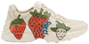 Gucci women’s Rhyton sneaker in white leather featuring oversized Gucci Strawberry graphic and chunky retro sole.

